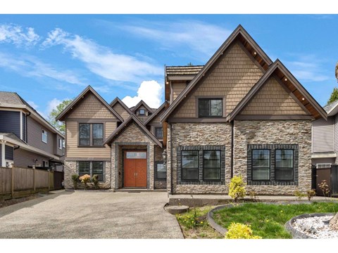 A house with a brown roof and a stone wall is surrounded by a fence and has a driveway.