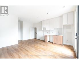 A room with wooden floors and white walls, with a set of white cabinets on the wall.