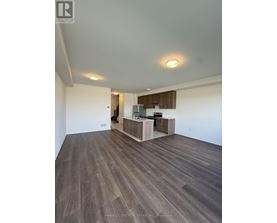 A spacious room with wood flooring and a kitchen area in the background.