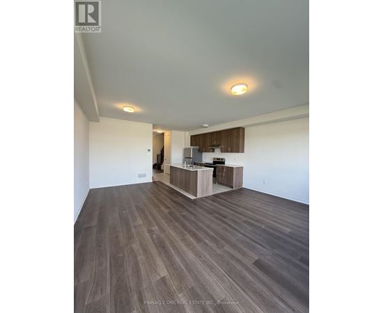 A spacious room with wood flooring and a kitchen area in the background.
