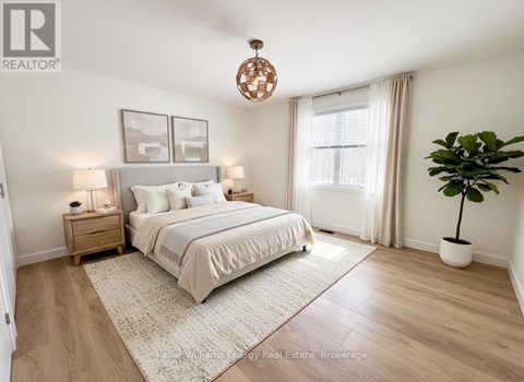 A bedroom with a large bed, a nightstand with a lamp, a window with curtains, and a potted plant.