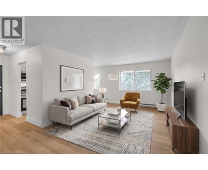 A living room with a grey couch, a brown armchair, a glass coffee table, a television, and a potted plant.
