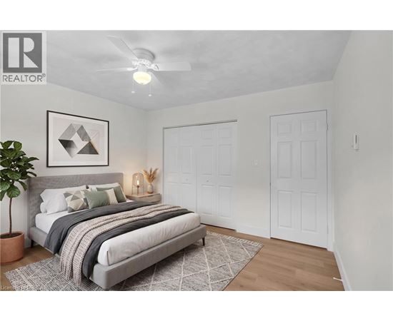 A bedroom with a bed, a plant, and a framed picture on the wall.
