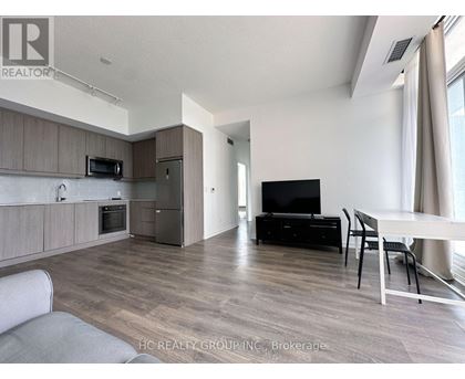 A modern living room with a grey sofa, a black TV, and a dining table with chairs.