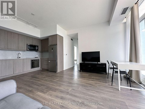 A modern living room with a grey sofa, a black TV, and a dining table with chairs.