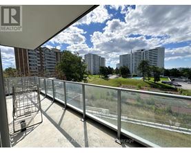 A balcony with a metal railing overlooks a grassy area and buildings.