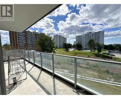 A balcony with a metal railing overlooks a grassy area and buildings.
