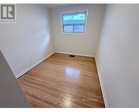 A room with wood flooring and a window showing a view of a building.