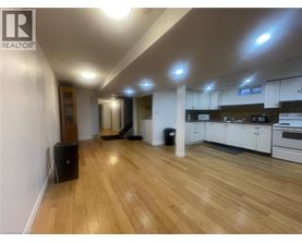 A well-lit, spacious room with wooden flooring and a kitchen area with white cabinets.