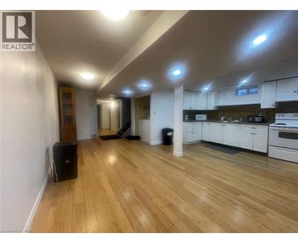 A well-lit, spacious room with wooden flooring and a kitchen area with white cabinets.