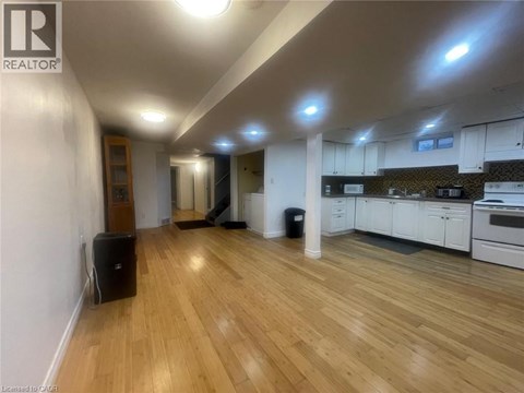 A well-lit, spacious room with wooden flooring and a kitchen area with white cabinets.