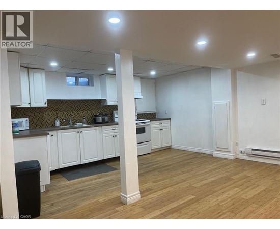 A well-lit, empty kitchen and living room with wooden floors and white walls.