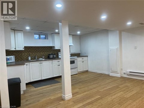 A well-lit, empty kitchen and living room with wooden floors and white walls.