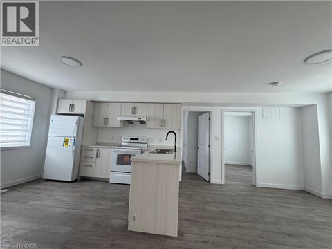 A well-lit kitchen with a refrigerator, oven, and sink.