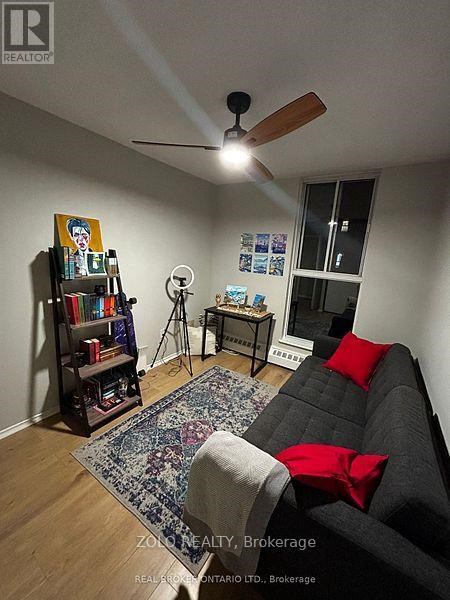 A living room with a grey couch, a rug, a bookshelf, and a ceiling fan.