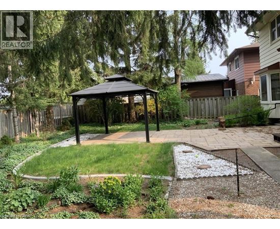A gazebo is in the middle of a garden with a gravel area in front of it.