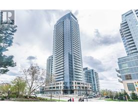 A tall, modern glass building stands in front of two other buildings on a cloudy day.