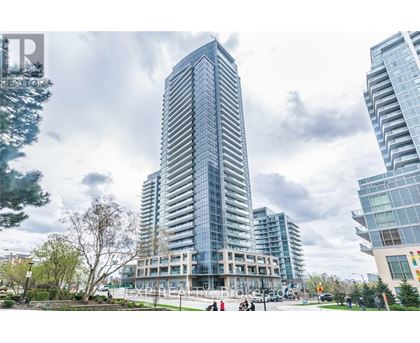 A tall, modern glass building stands in front of two other buildings on a cloudy day.
