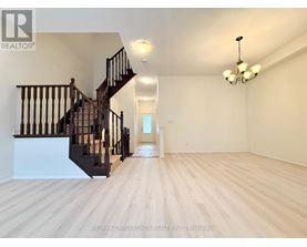 A spacious room with wooden flooring and a staircase with black railings.