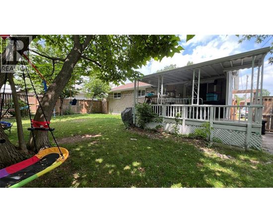 A backyard with a swing set and a surfboard leaning against a tree.