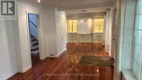 A spacious room with wooden floors and white walls, featuring a staircase and a row of windows.