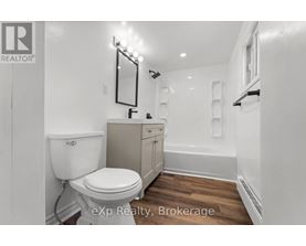 A white toilet is in a small bathroom with wood flooring.