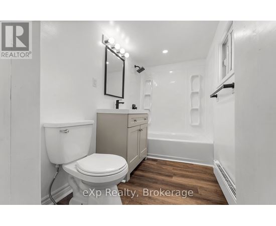 A white toilet is in a small bathroom with wood flooring.