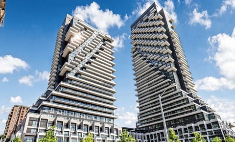 Two modern high-rise buildings with balconies and windows are set against a blue sky with clouds.
