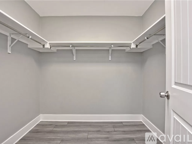 A white door is on the right side of a room with a grey floor and white walls.