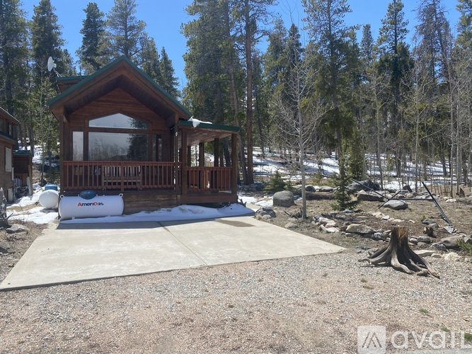 A wooden cabin with a porch and a covered patio is surrounded by trees and snow.