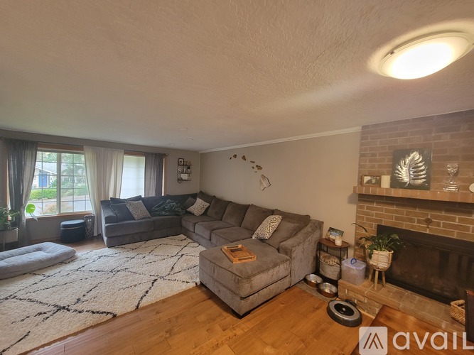 A living room with a grey couch, a white rug, and a fireplace.