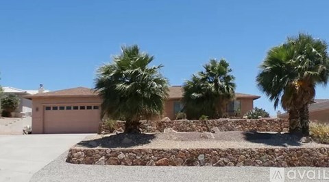 A house with a stone wall and palm trees in front.