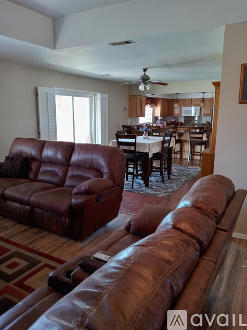 A living room with brown leather furniture and a dining area in the background.