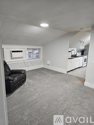 A living room with a black leather couch and a grey carpet.
