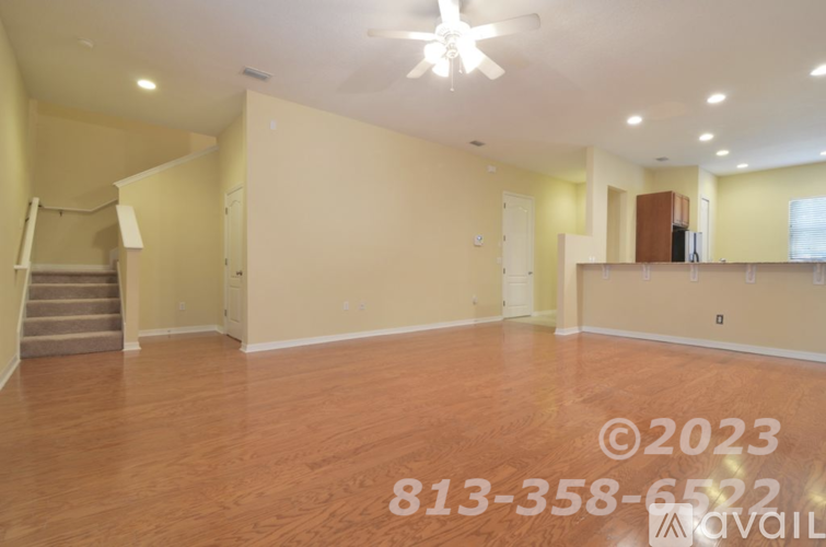 A spacious room with wooden flooring and a staircase on the left side.