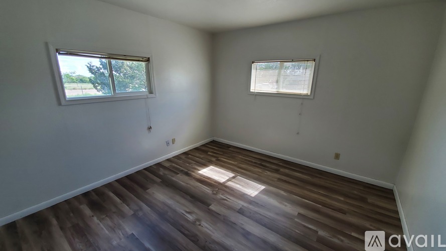 A room with wooden flooring and two windows.