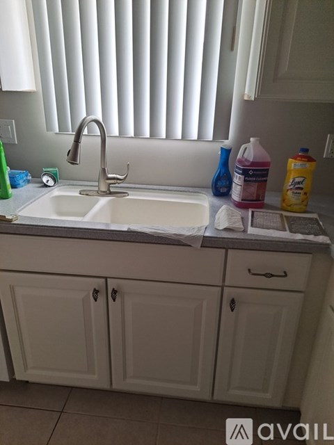 A kitchen sink with a white counter top and white cabinets.