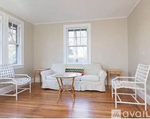 A living room with a white couch, two white chairs, and a round table with a woven base.