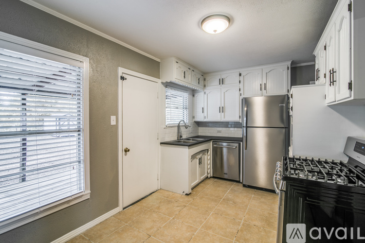 A kitchen with a stainless steel refrigerator, a stove, and white cabinets.