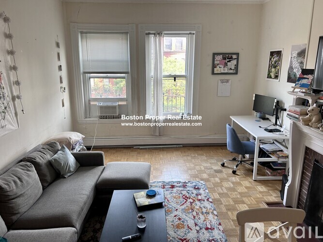 A living room with a grey couch, a fireplace, and a desk with a computer.