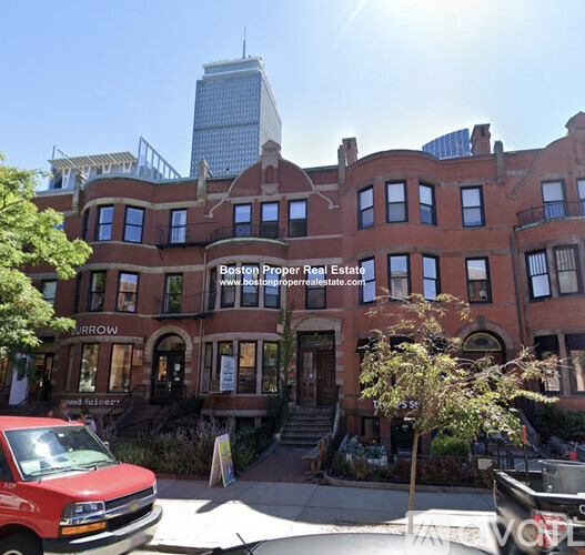 A red truck is parked in front of a building with a sign that says "Boston Proper Real Estate.".