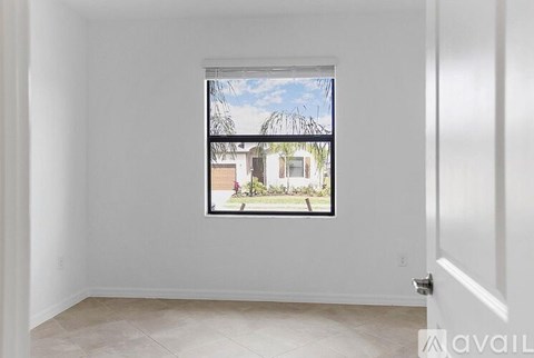 A room with a window showing a view of a house and trees.