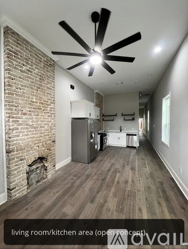 A living room and kitchen area with a brick wall and wood flooring.