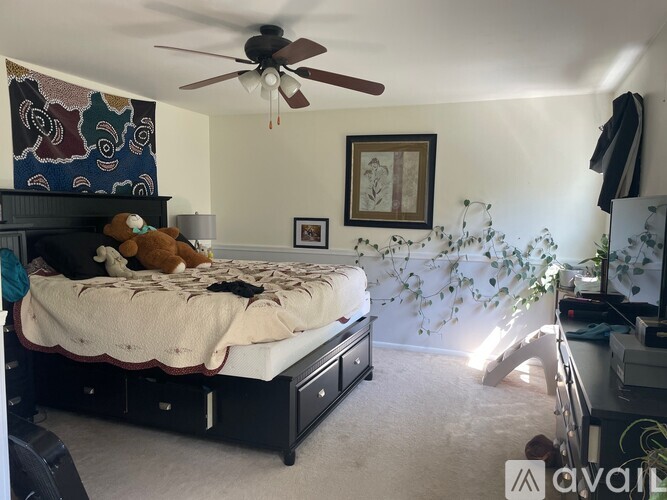 A bedroom with a bed, a ceiling fan, and a wall hanging.