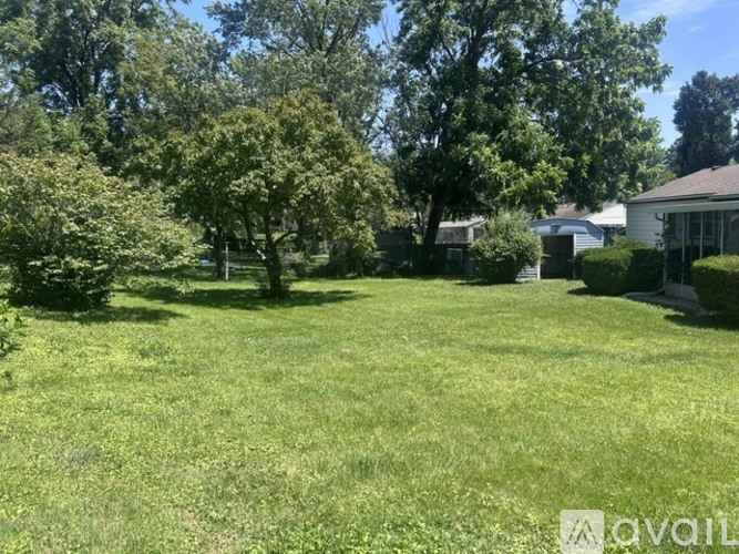 A grassy backyard with trees and a house in the background.