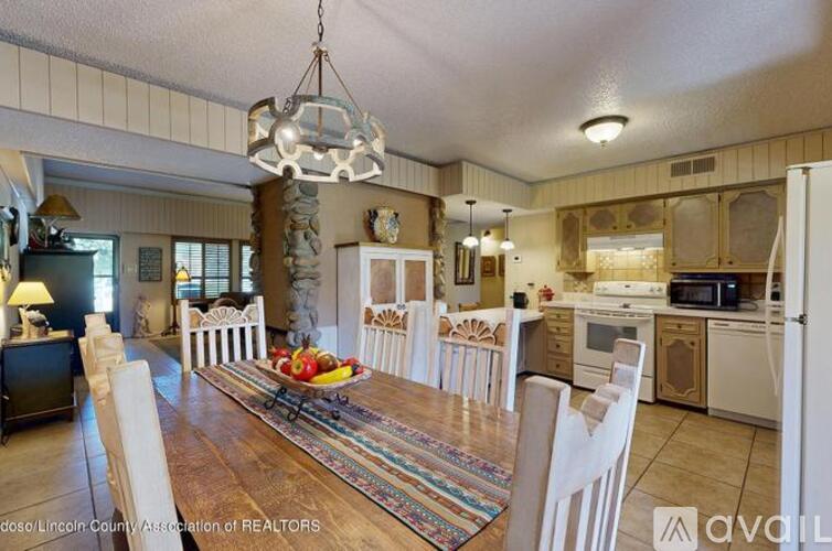 A well-lit kitchen with white chairs and a wooden table.