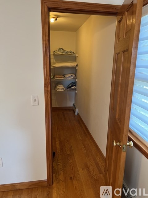A hallway with a doorway leading to a bedroom with a bed and a shelf.