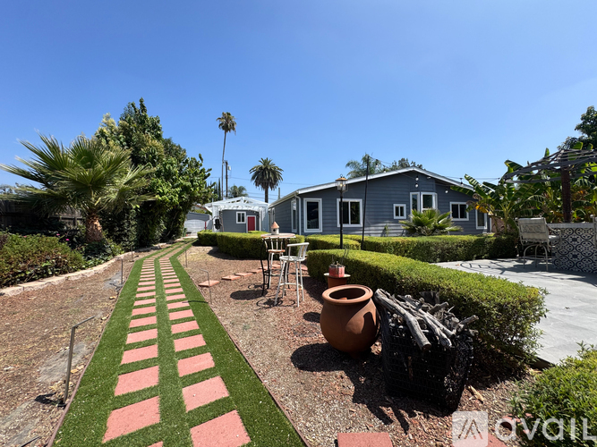 A house with a blue exterior is surrounded by a garden with a red and green striped path.