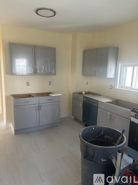 A kitchen with grey cabinets and a black trash can.