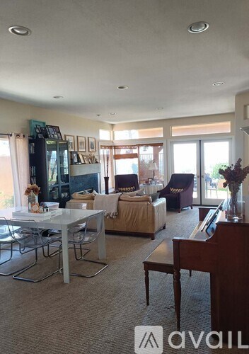 A living room with a white dining table and chairs, a couch, a piano, and a vase of flowers.